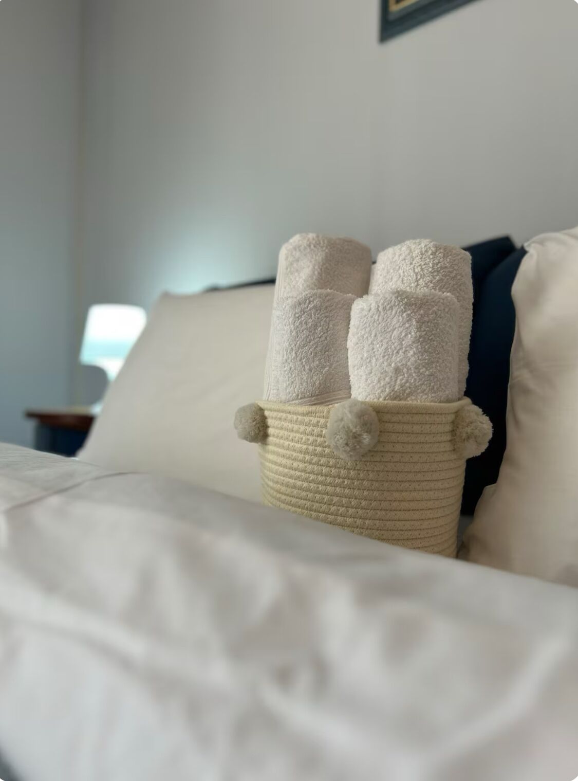 Un lit avec du linge de lit blanc et un panier en osier contenant trois serviettes blanches.