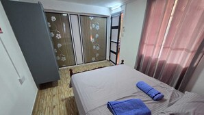 Habitación con cama, dos almohadas, una toalla azul, suelo de madera, armario y puerta corrediza con motivos florales.