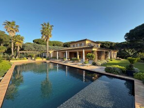 Une grande maison à deux étages, avec une piscine en premier plan.