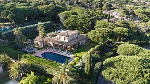 A large, multi-story house with a swimming pool, surrounded by lush greenery and trees.