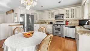 A kitchen with white cabinets, stainless steel appliances, a dining table with a white tablecloth, and a chandelier.