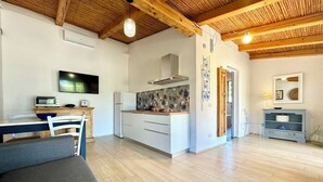 A modern kitchen with white cabinets, a built-in oven, and a microwave. There is a dining area with a table and chairs, and a living room with a sofa. - "Le Corti Sarde Sea Breeze" (Bari Sardo)