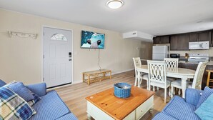 En stue med sofasæt, et træbord, et spisebord med stole, et køkken med en mikrobølgeovn og en dør med dekorativt glas.