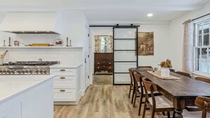 A modern kitchen with white cabinetry, a gas stove, and a wooden dining table with chairs. - Woodstock Way Ranch on Private Wooded Acres (Woodstock)