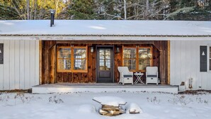 A cabin with a wooden exterior, a front door, two wicker chairs, and a small table. - Woodstock Way Ranch on Private Wooded Acres (Woodstock)