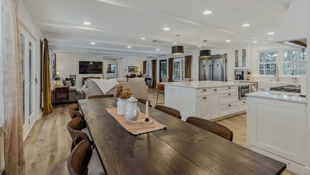 A modern kitchen with white cabinets, a wooden dining table, and a large island. - Woodstock Way Ranch on Private Wooded Acres (Woodstock)