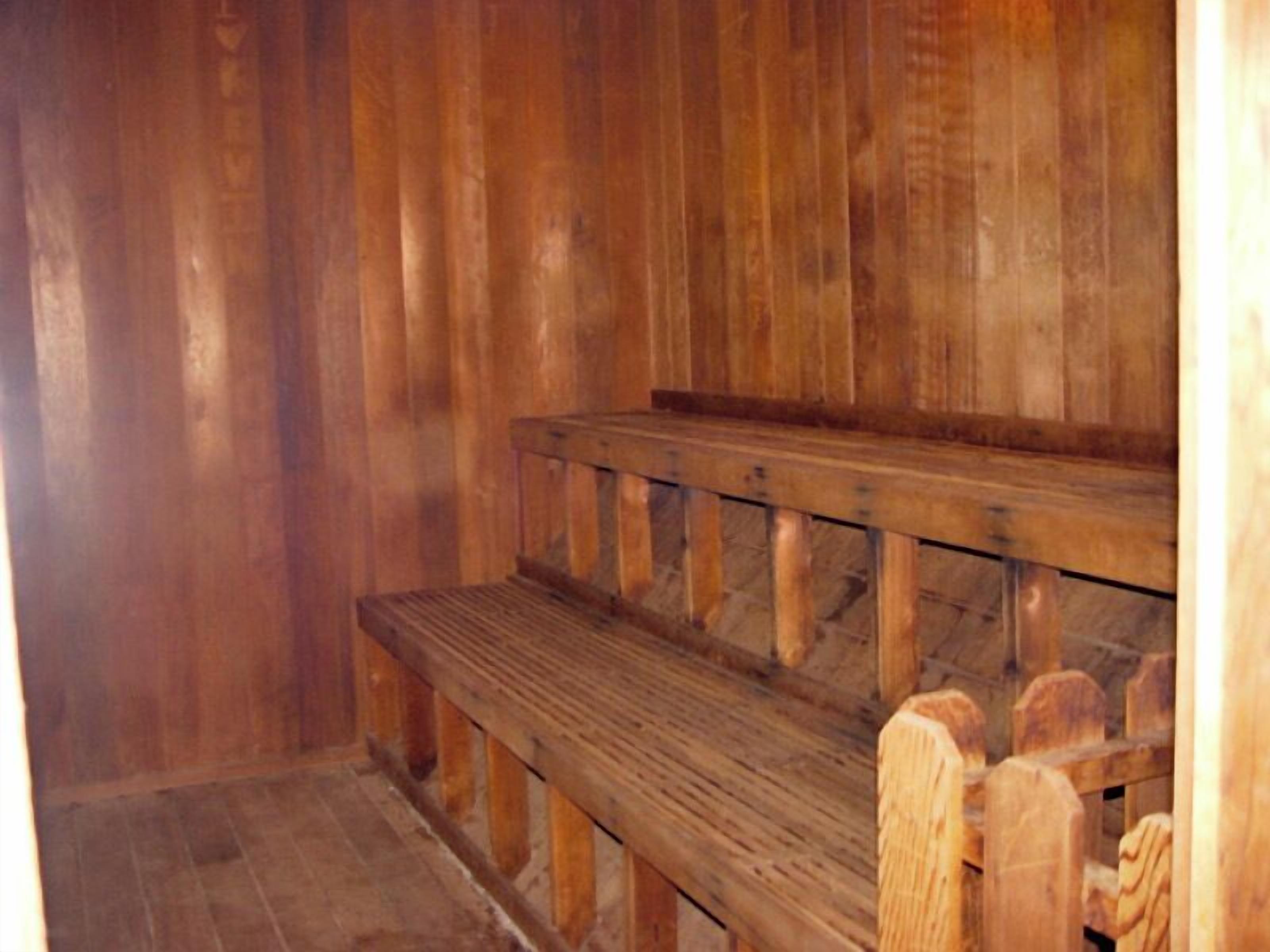 A wooden bench with a slatted seat and backrest, positioned against a wooden wall.