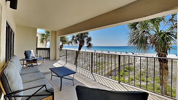 Un balcon donnant sur la plage, aménagé avec un canapé, des chaises et une table.