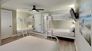 A room with bunk beds, a ceiling fan, and a mounted TV. - Easy on Eastern Lake | Pet Friendly Luxury Townhome (Santa Rosa Beach)