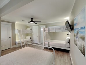 Una habitación con literas, ventilador de techo y televisión montada en la pared.
