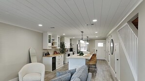 A modern kitchen with white cabinetry, a central island, and a dining area with bar stools. - Easy on Eastern Lake | Pet Friendly Luxury Townhome (Santa Rosa Beach)