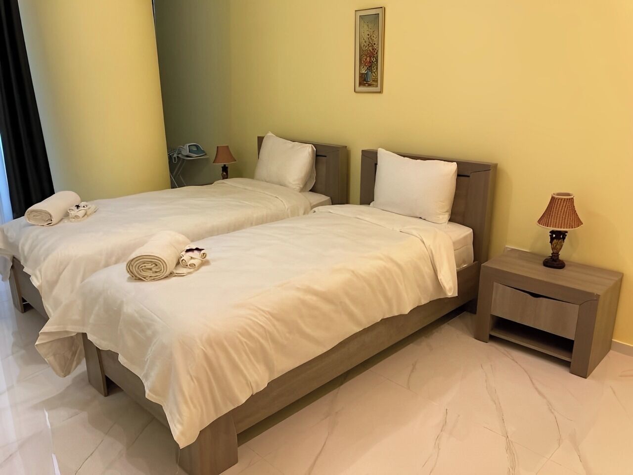 Een hotelkamer met twee bedden, een nachtkastje met een lamp en een schilderij aan de muur.