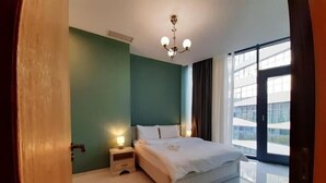 Habitació d'hotel moderna amb un llit gran, una tauleta de nit amb una làmpada, una làmpada al sostre i vista a la ciutat a través de grans finestres.