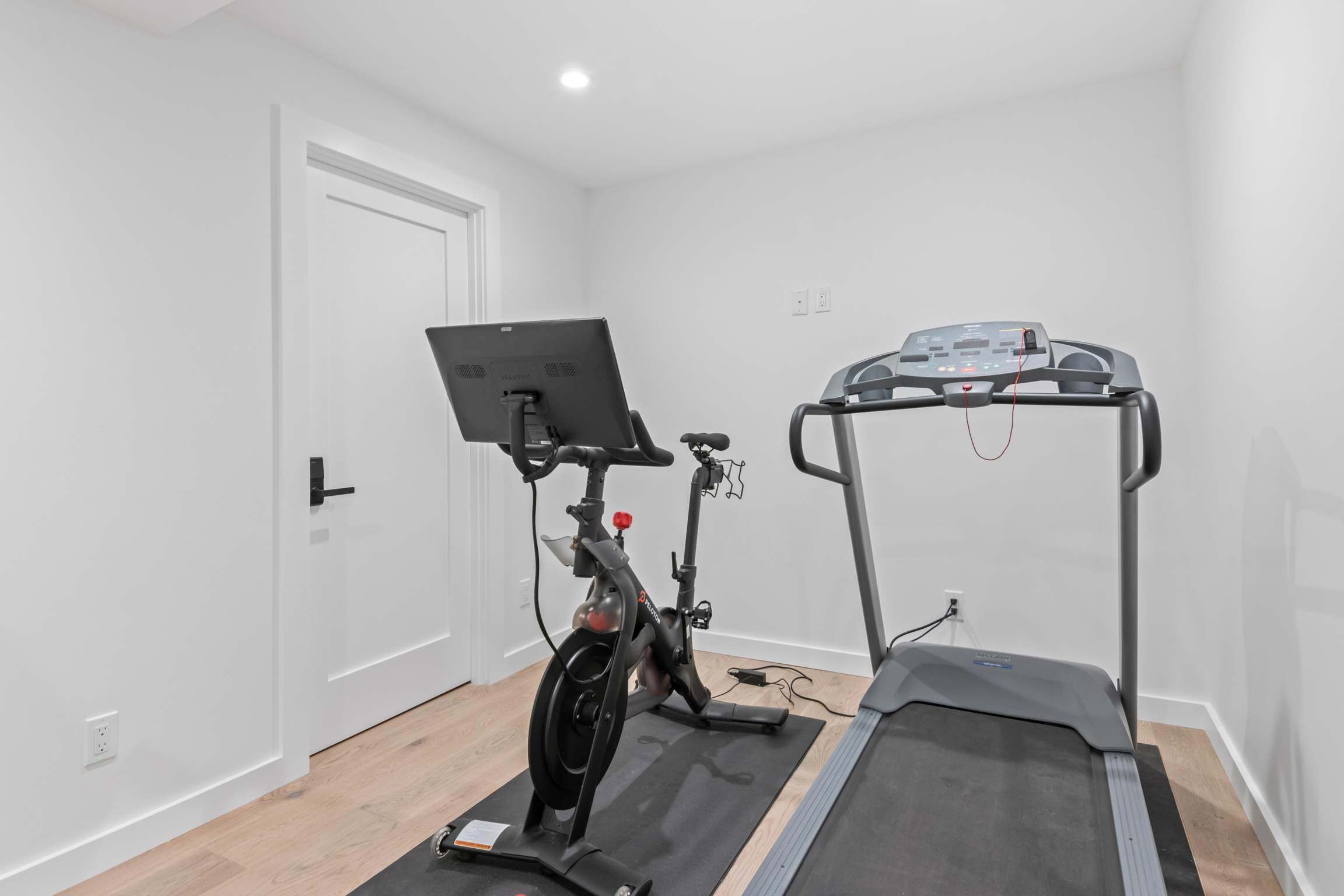 A room with a stationary bike, a treadmill, and a door.