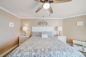 A bedroom with a large bed, two bedside tables, a ceiling fan, and a decorative wall piece.