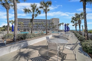 Ein Poolbereich eines Resorts mit Palmen, einem großen Gebäude im Hintergrund und blauem Himmel.