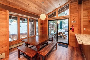 Cozy cabin interior with a large dining table and benches, offering a view of the surrounding landscape.