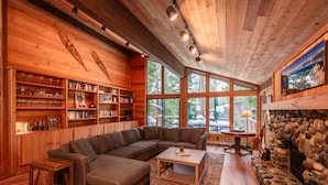 Een gezellige woonkamer met een grote hoekbank, houten boekenkasten en een stenen open haard.