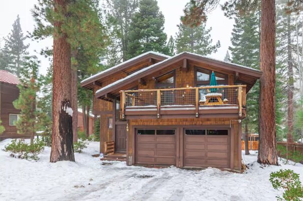 Escape to a cozy cabin nestled in a snowy forest, offering a balcony with a railing and a covered outdoor seating area.