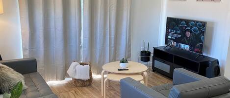 A modern living room with a grey sofa, a small round table, a TV, and a potted plant.