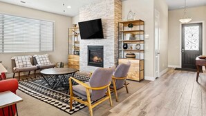 Una sala de estar con chimenea, televisor montado en la pared, sofá, dos sillones y una mesa de centro.