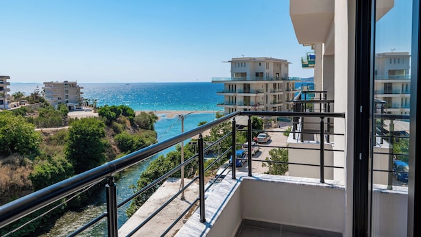 A balcony with a view of the sea, a parking area, and adjacent buildings. - Cuni Luxury Hotel (Sarandë)