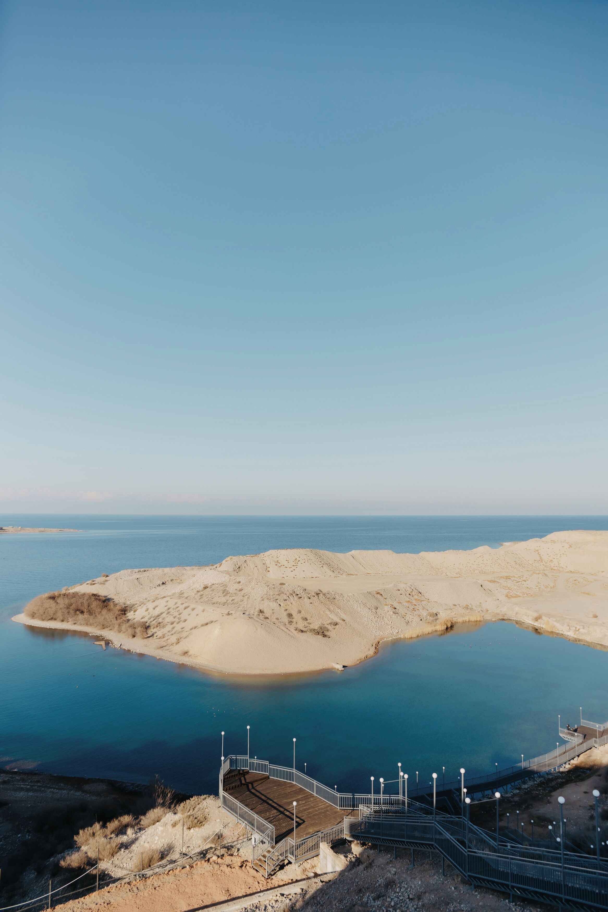 A coastal landscape with a clear sky, a sandy beach, and a calm body of water.
