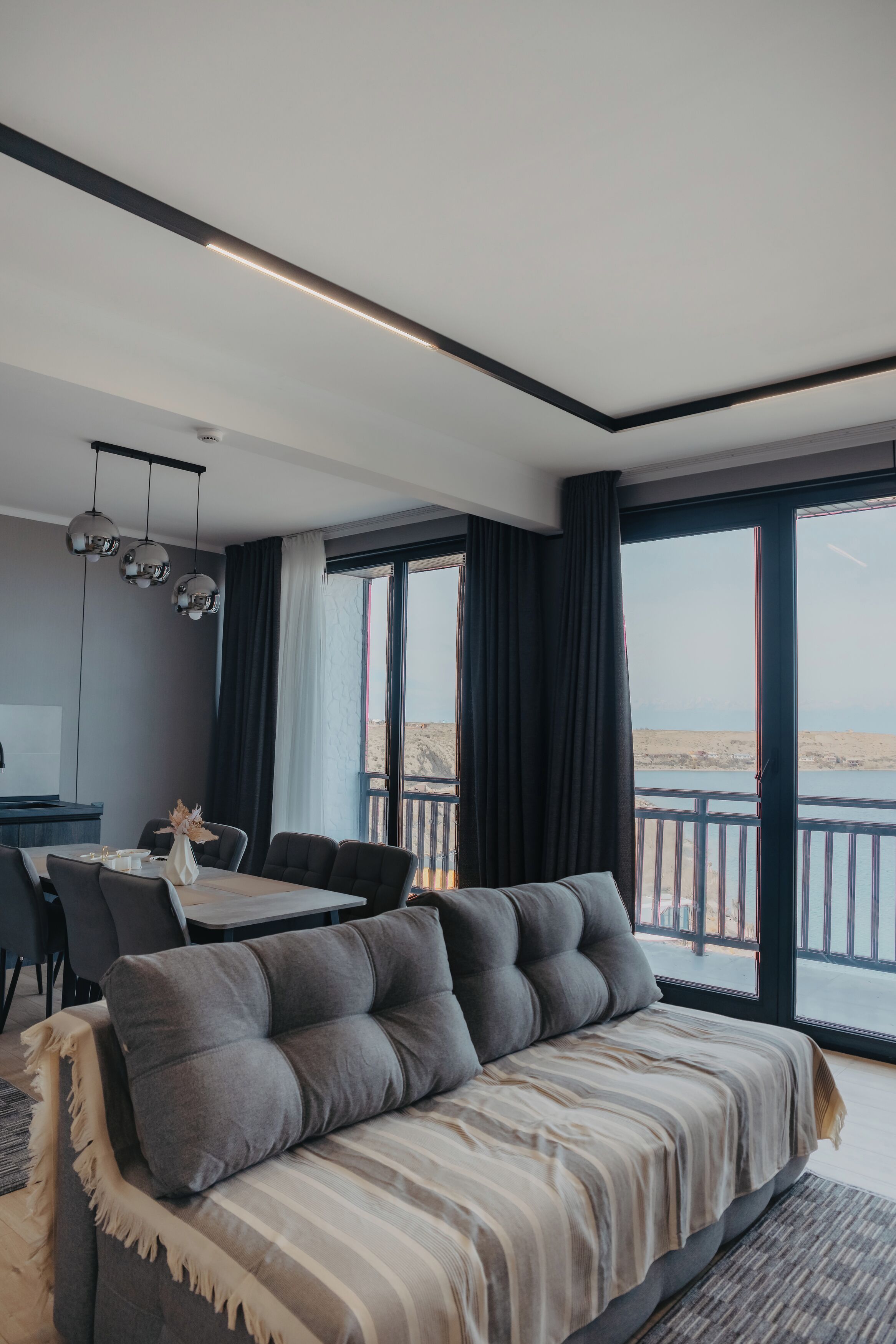 Quarto moderno com sofá, mesa de jantar e cadeiras. Ampla janela com vista para o exterior.
