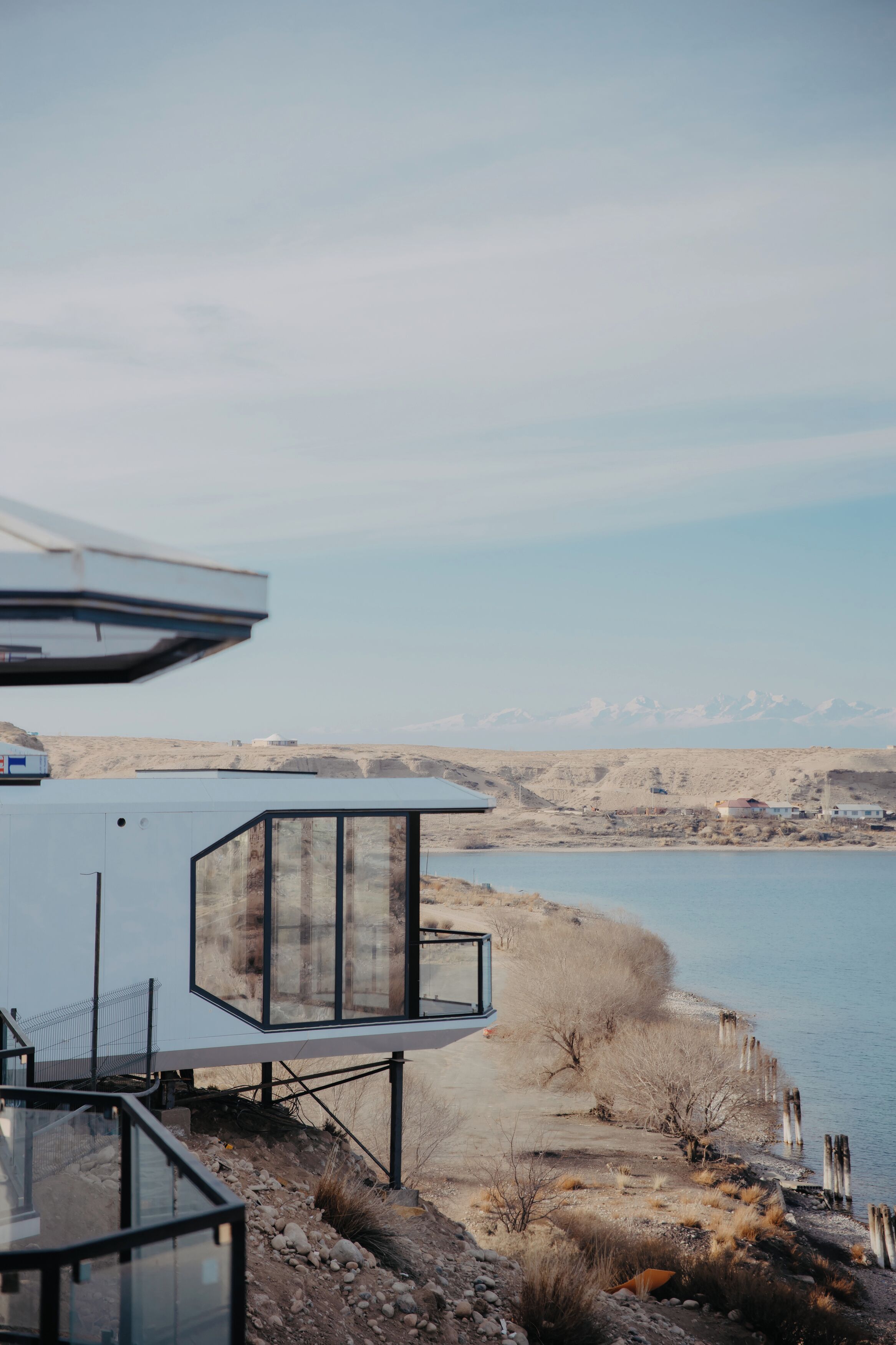 Un edificio moderno con amplios ventanales de vidrio que dan a una masa de agua y un paisaje montañoso.