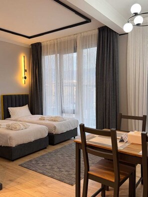 A hotel room with two beds, a dining table, and a chandelier.