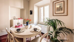 Zona pranzo con tavolo rotondo, sedie, un vaso con fiori e un quadro appeso al muro.