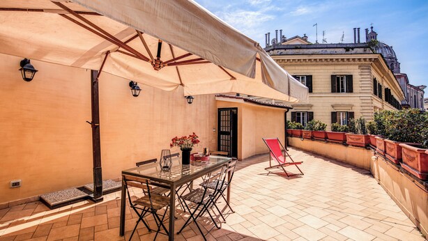 Un patio esterno con tavolo e sedie, una zona riparata e vista su un edificio storico.