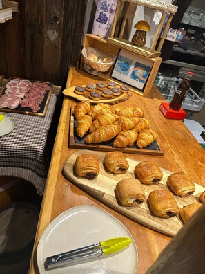 Ein reichhaltiges Frühstücksbuffet mit verschiedenen Backwaren, darunter Croissants und Schokoladenpasteten, sowie einer Auswahl an Fleisch- und Käsesorten.