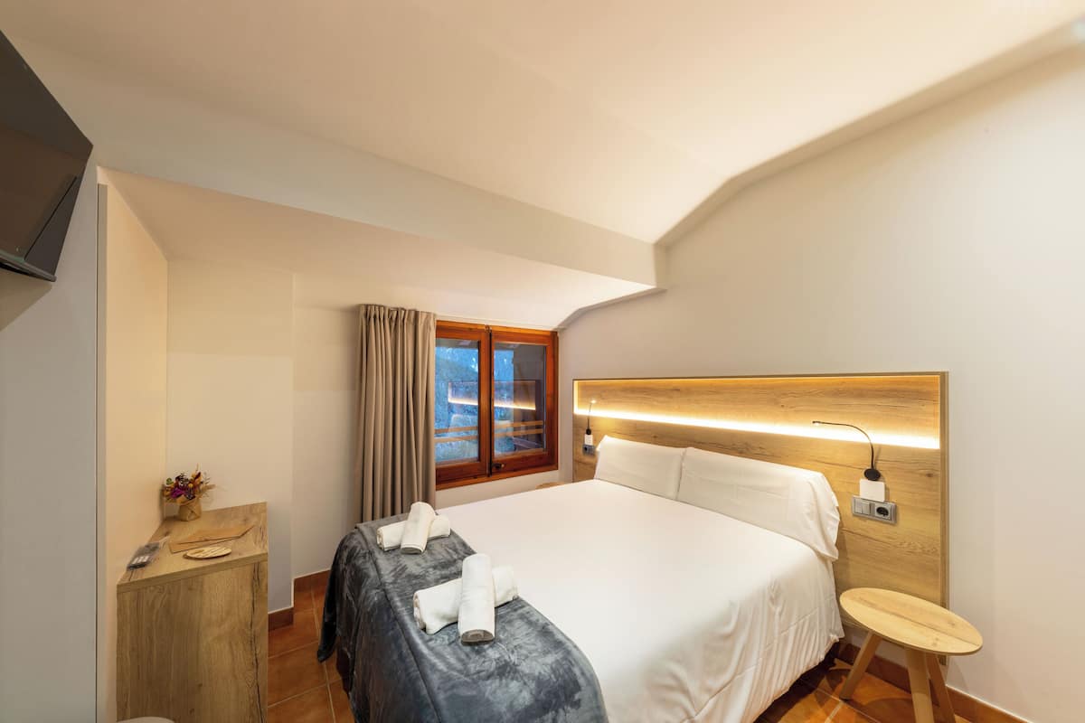 A hotel room with a bed, bedside table, and a window with curtains.