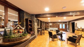 A spacious living area with a stone fireplace, wooden beams, and a dining table with chairs. - Hotel Restaurant Camp del Serrat (Escaldes-Engordany)