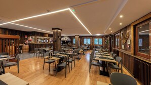 A spacious restaurant with wooden floors and tables, a bar area with bottles and decorations, and large windows allowing natural light. - Hotel Restaurant Camp del Serrat (Escaldes-Engordany)