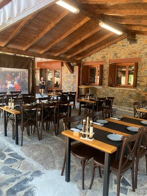 Ein Essbereich im Freien mit Steinmauern und Holzbalken, Tische mit Stühlen und Blick auf ein nahegelegenes Restaurant.