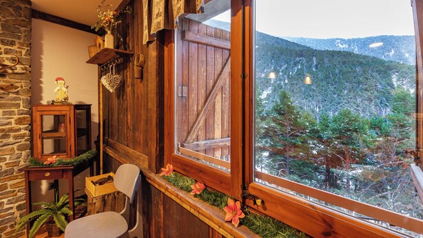 A rustic room with a wooden chair, a small table with a vase, and a window overlooking a forested mountain. - Hotel Restaurant Camp del Serrat (Escaldes-Engordany)