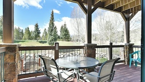 A covered outdoor area with a table and chairs, stone pillars, and a view of a grassy landscape with trees.