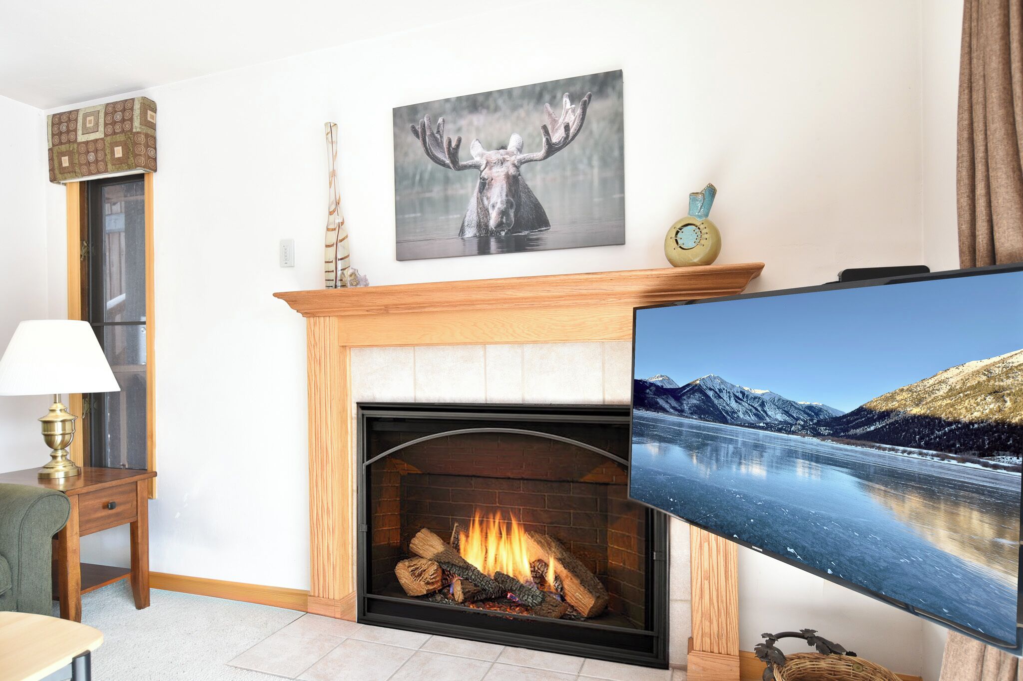Una sala de estar con chimenea, televisor montado y un cuadro de un alce.