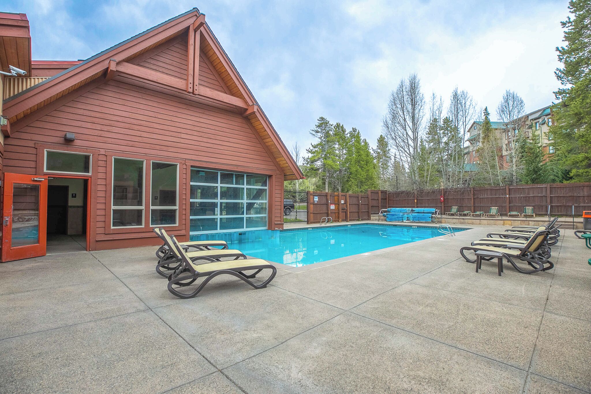 A pool area with lounge chairs and a wooden building with large windows.