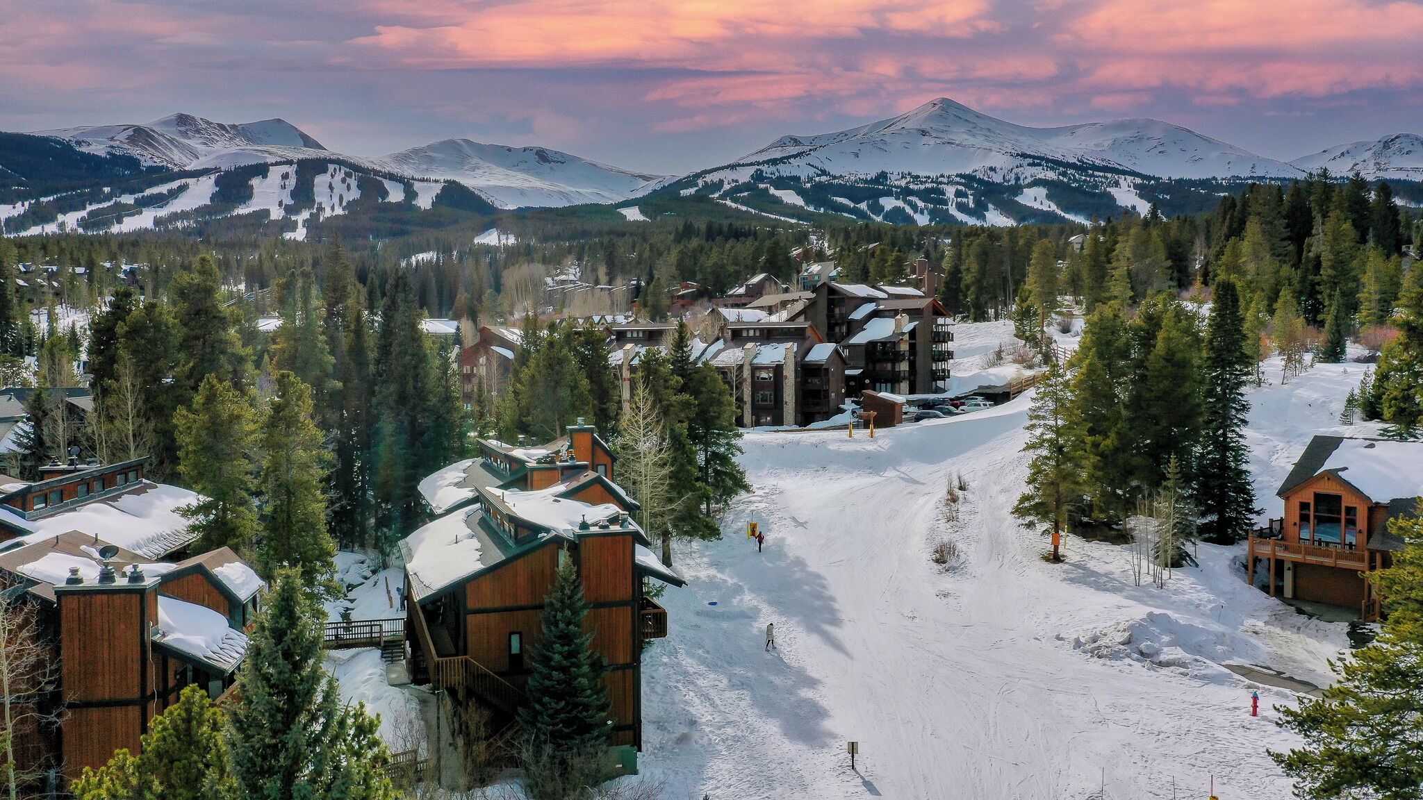 A snow-covered mountain resort with wooden buildings, ski slopes, and a backdrop of snow-capped peaks.