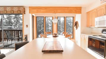 Una cocina moderna con una isla grande, armarios de madera y vistas a árboles cubiertos de nieve.