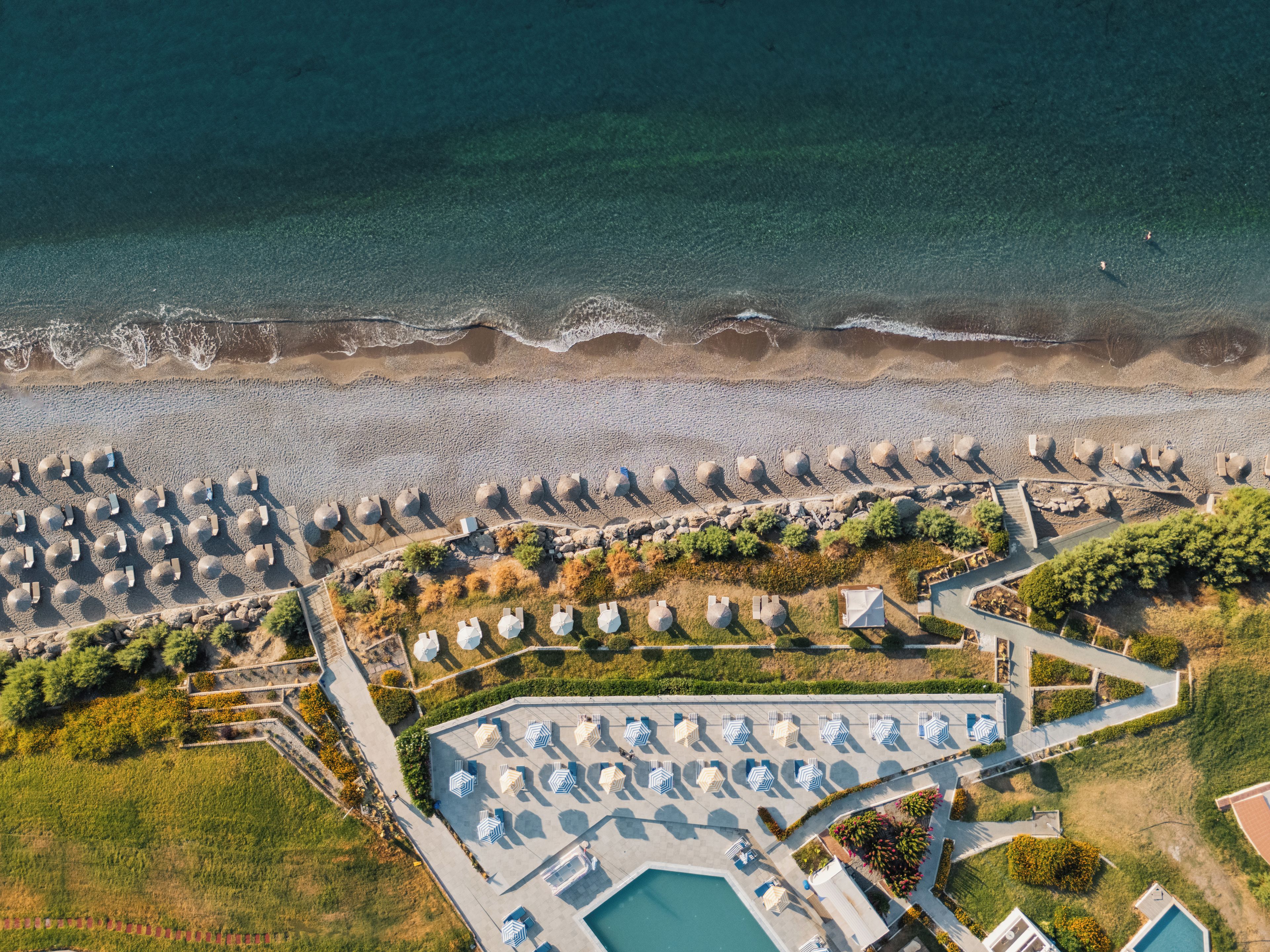 An aerial view of a coastal resort with a beach, umbrellas, and a swimming pool.