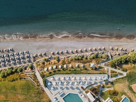 Vista aérea de un complejo turístico frente al mar, con playa, sombrillas y piscina.