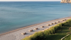 A beach with rows of sun loungers and a rocky cliff in the background.