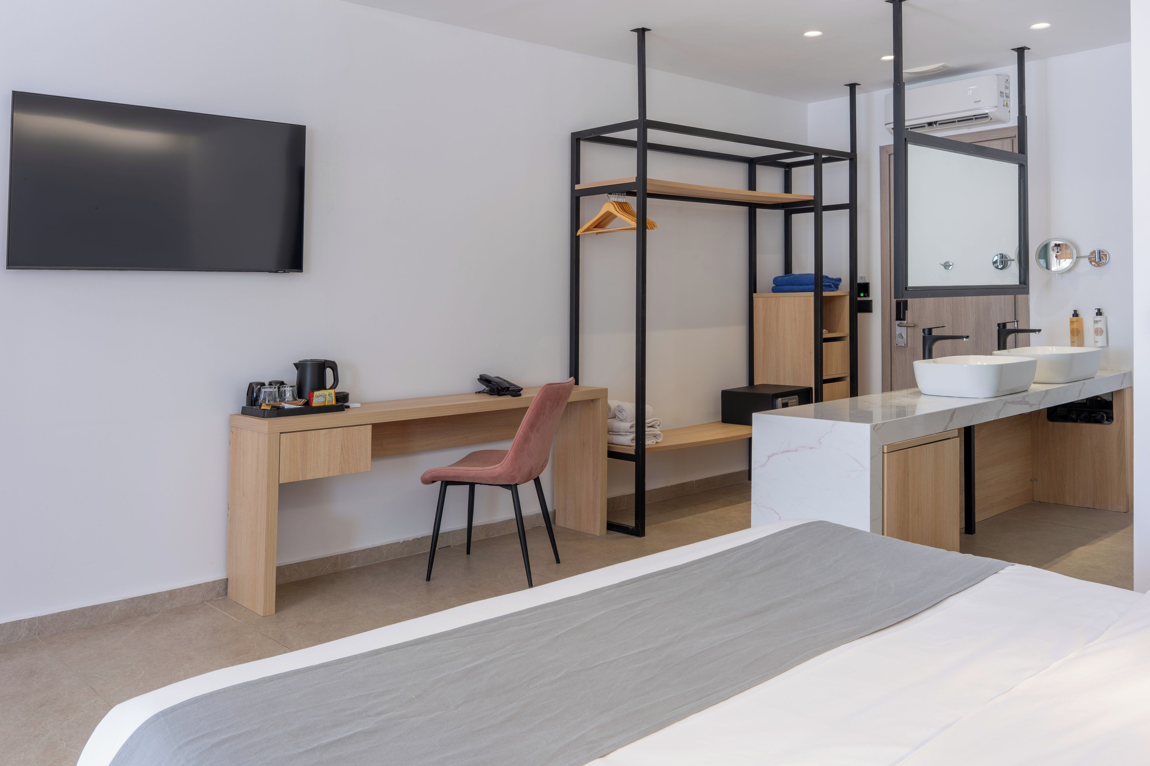 Ein modernes Hotelzimmer mit Bett, Schreibtisch, Stuhl, Fernseher und einem Badezimmer mit Spiegel sowie einem Hängehandtuchhalter.