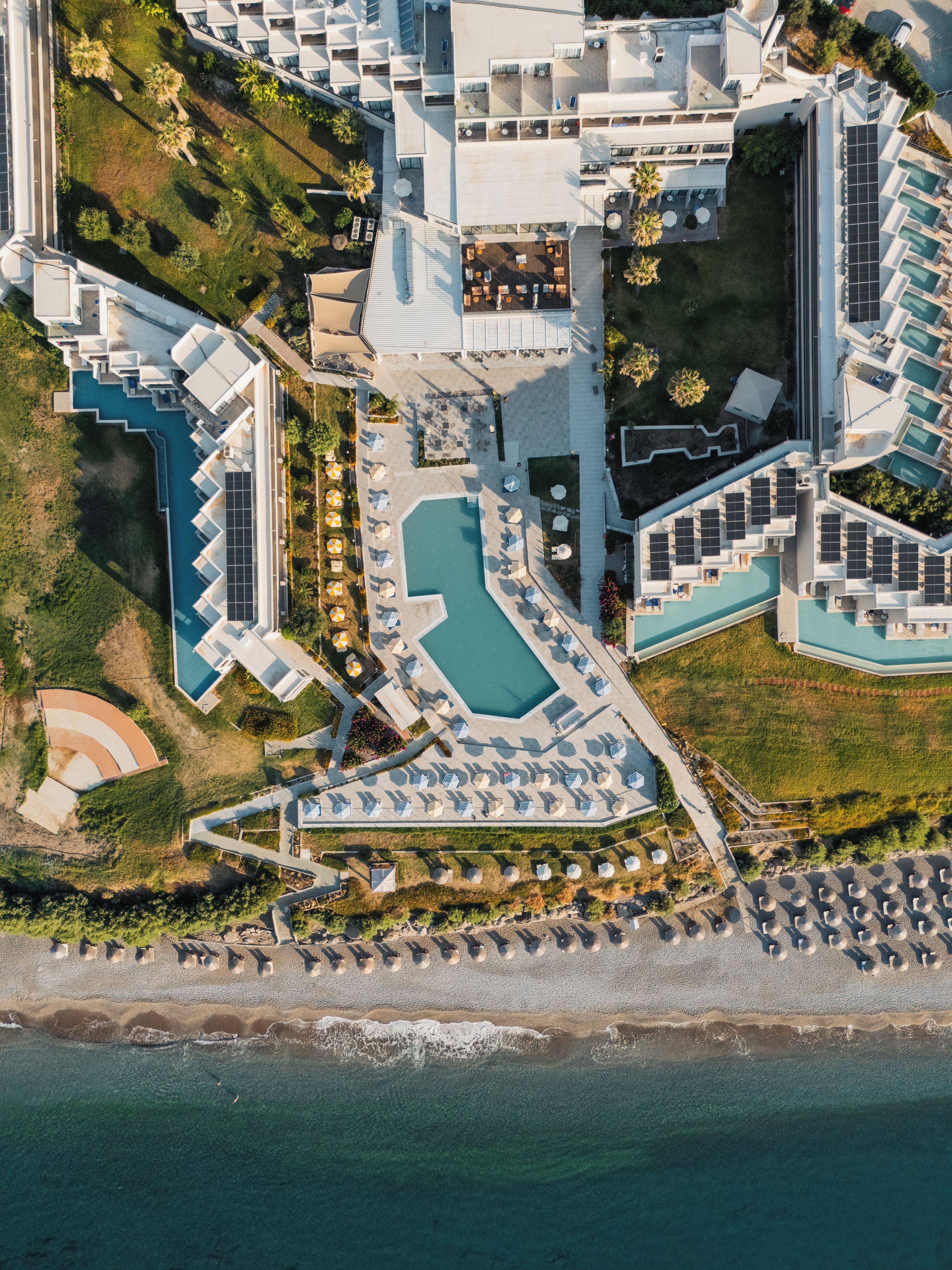 An aerial view of a resort with multiple swimming pools, sun loungers, and a beach area.