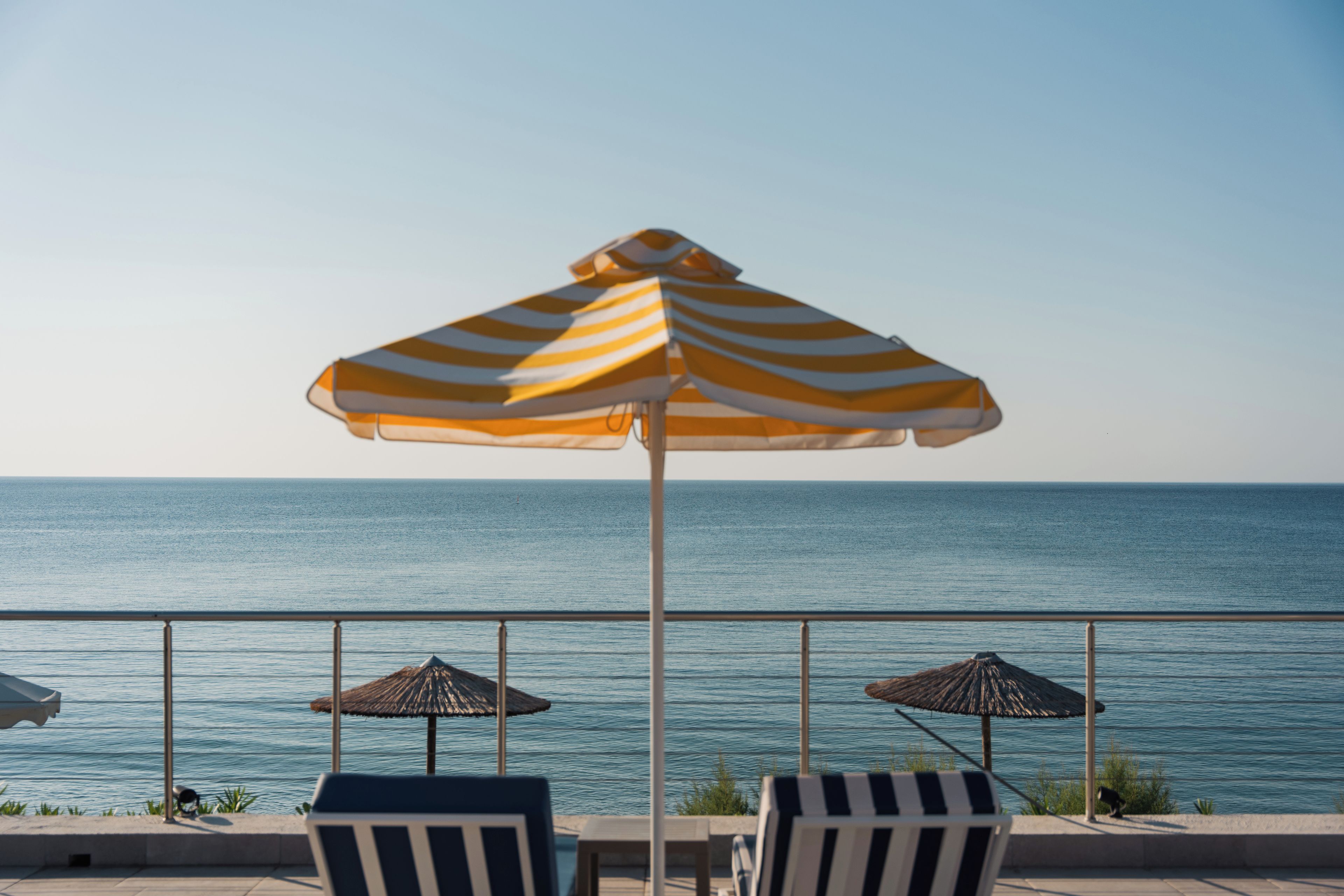 Une terrasse en bord de mer, agrémentée de parasols à rayures et de chaises longues, d’où l’on a une vue sur l’océan.