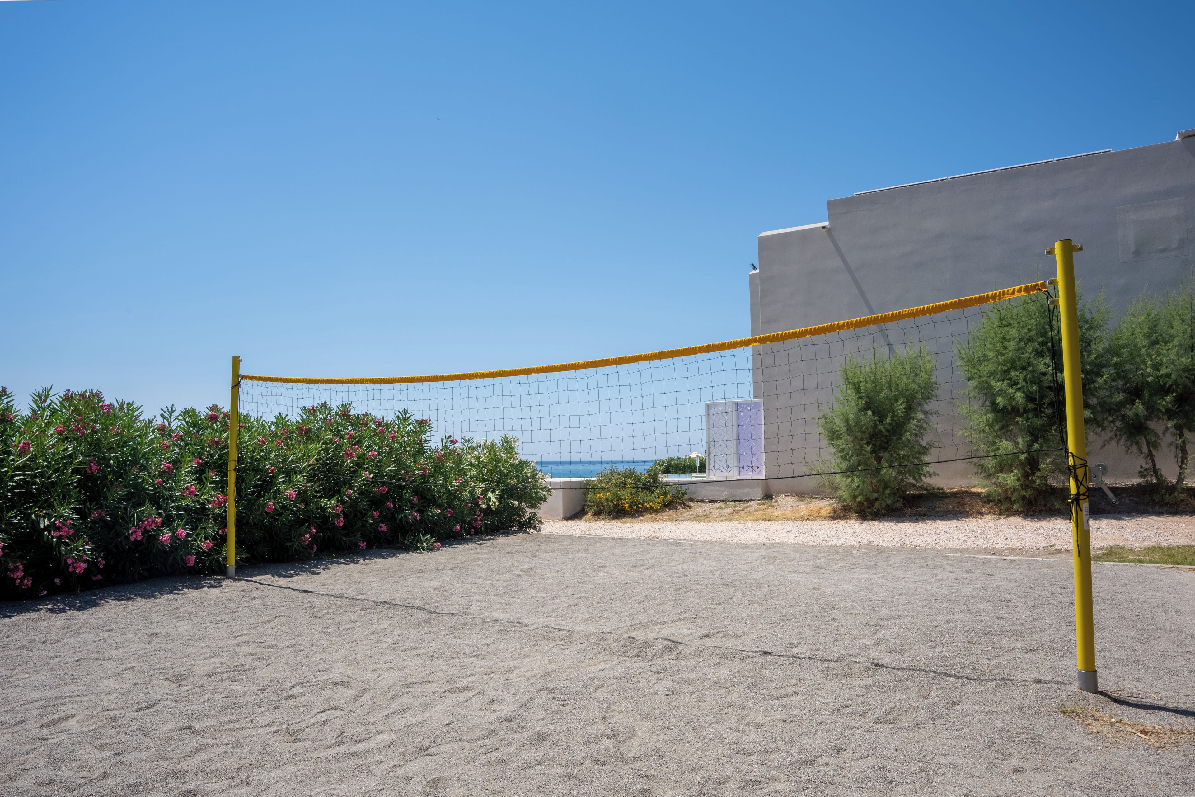 A volleyball net in a sandy area with a building and a view of the sea in the background.